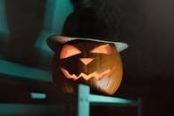 Carved jack-o'-lantern wearing a hat, glowing ominously in the dark, perfect for Halloween themes.